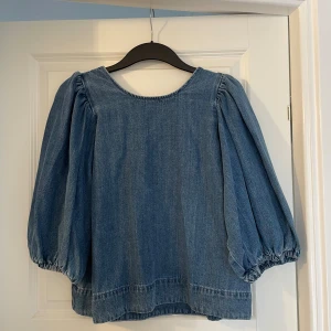 Jeansblus med puffärm från Zara - Säljer en snygg jeansblus från Zara i storlek L. Blusen har puffiga trekvartsärmar med resår vid ärmslut och en djup, rundad rygg. Tillverkad i klassiskt blått jeanstyg som ger en cool och avslappnad vibe. Perfekt för dig som gillar statement-ärmar och denim.