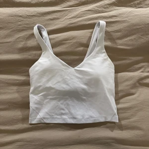 Ljusblått/lila topp  från Lululemon - Säljer en ljusblå/lila topp från Lululemon med v-ringning och breda axelband. Toppen är croppad och har en stilren, enkel design med Lululemons logga på ryggen. Perfekt för träning eller chill dagar. Materialet är mjukt och stretchigt för maximal komfort. Har kortet man får när man köper toppen 