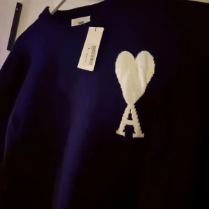 Mörkblå stickad tröja från Ami  - Snygg mörkblå stickad tröja från Ami Alexandre Mattiussi med vit hjärtlogga och bokstaven A på bröstet. Tröjan har rund halsringning, ribbade muddar och lång ärm. Perfekt för dig som gillar stilrena och trendiga plagg. Passar som m eller s lite oversize 