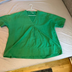 Grön v-ringad blus från Marc O'Polo - Snygg grön blus från Marc O'Polo i 100% ekologisk bomull. Modellen har v-ringning, korta ärmar och en lös passform med lätt rynk framtill. Perfekt för dig som gillar en enkel men stilren look.