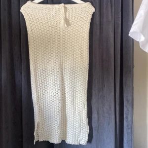 Vit stickad långklänning FB Sister XS - Superfin vit stickad långklänning från FB Sister i storlek XS. Klänningen har ett snyggt virkat mönster, knytband med tofsar i midjan och är perfekt för sommarens varma dagar. Den är lång och har en avslappnad passform som känns både trendig och bekväm.