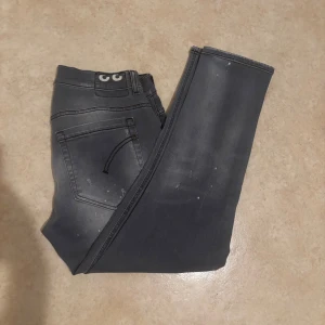 Grå slitna jeans i storlek 33 - Säljer ett par grå jeans med slitningar och hål för en riktigt edgy look. Jeansen har smal passform och klassisk femficksdesign. Snyggt tvättade detaljer och coola slitningar framtill ger en streetkänsla. Perfekta för dig som gillar en rå och avslappnad stil.