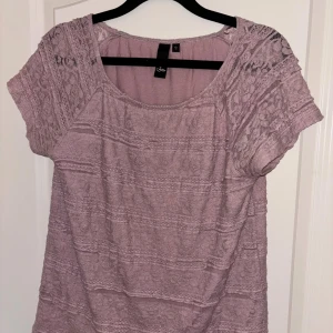 Ljuslila spetsblus med kort ärm - Superfin ljuslila blus från Sisters Point med korta ärmar och vackra spetsdetaljer över axlar och ärmar. Blusen har rund halsringning och ett romantiskt mönster i spets över hela plagget. Perfekt för dig som gillar en söt och feminin stil.