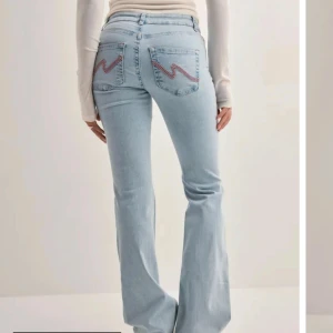 Ljusblå nelly jeans bootcut - Snygga ljusblå lågmidjade jeans med bootcut passform och slitna detaljer vid knäna. Jeansen har klassiska bakfickor med cool rosa zigzag-söm och ätillverkade i mjukt denim. Perfekta för en avslappnad och trendig look. Knappt andvänt. 💕