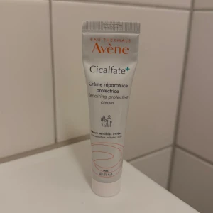 Avène Cicalfate+ skyddande kräm - Avène Cicalfate+ är en vit skyddande och reparerande kräm i tub på 40 ml, men ungefär 30ml kvar. perfekt för känslig och irriterad hud. Tuben är smidig att ta med och har en enkel design med orange och blå text. Krämen är parfymfri och passar dig som vill lugna huden snabbt.