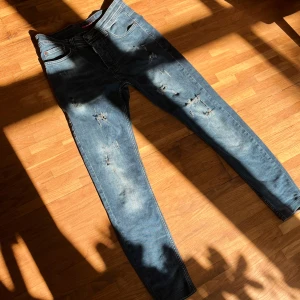 Dsquared2 jeans - Snygga blå jeans från Dsquared2 med slitningar och distressed detaljer. Modellen har klassisk femficksdesign, knappgylf och smal passform. Jeansen är tillverkade i bomull och har en cool, modern look med tydliga slitningar på benen.