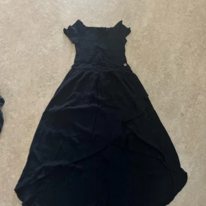 Marinblå långklänning från Kappahl - Supersöt marinblå långklänning från kappahl med volangärmar och omlottkjol. Klänningen har smockad överdel och en liten dekorativ knapp i midjan. Perfekt för dig som gillar en flowy och elegant stil.