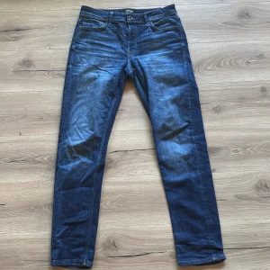 Jack & Jones blå tapered jeans - Säljer ett par blå jeans från Jack & Jones i modellen Tapered/Mike. Jeansen har klassisk femficksdesign, normalhög midja och avsmalnande ben. Materialet är mjukt denim i bomull med lite stretch för extra komfort. Perfekta för dig som gillar en avslappnad men ändå snygg look.