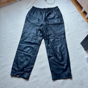 Svarta skinnbyxor med resårmidja - Säljer ett par svarta skinnbyxor med resår i midjan och raka ben. Byxorna har sidfickor och är fodrade på insidan för extra komfort. Perfekta för dig som vill ha en edgy och stilren look.