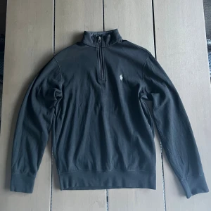 Svart half zip tröja från Polo Ralph Lauren - Svart långärmad tröja från Polo Ralph Lauren med klassisk broderad logga på bröstet. Tröjan har en ståkrage med half zip-dragkedja och är gjord i mjuk bomull. Perfekt för en clean och stilren look.