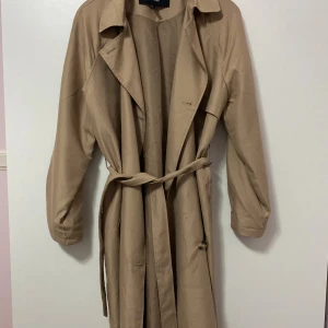 Beige trenchcoat från Vero Moda - Beige trenchcoat från Vero Moda med klassisk krage, knappar framtill och bälte i midjan. Använd ett par gånger med ett fåtal knappt synliga deffekter (sista bilden). Är i storlek S (dock väldigt oversized), pris kan diskuteras 🤗