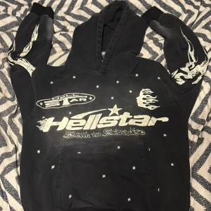 hellstar hoode - Svart hoodie från Hellstar med stora vita tryck fram och bak, inklusive flames, stjärnor och logga. Hoodien har huva, känguruficka och coola detaljer på ärmarna. Perfekt för dig som gillar streetwear med unik design.