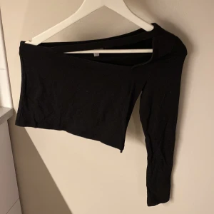 Svart oneshoulder topp från ASOS - Säljer en svart croppad topp från ASOS med en ärm och snygg oneshoulder-design, storlek 36. Toppen är tight och tillverkad i mjuk bomull, perfekt för dig som vill sticka ut med en stilren och edgy look.