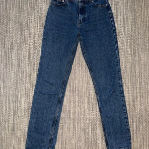 Blåa raka jeans från NLY Jeans - Klassiska blå jeans från NLY Jeans med hög midja och raka ben. Jeansen har fem fickor, silverfärgade knappar och dragkedja. Tillverkade i robust denim med snygga kontrastsömmar och patch bak i midjan.
