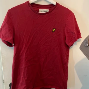 Röd t-shirt från Lyle & Scott - Röd t-shirt från Lyle & Scott i ekologisk bomull. Klassisk passform med rund hals och korta ärmar. På bröstet sitter den ikoniska gula loggan. Perfekt basic-plagg med stilren look. Använd antal gånger och tvättad så materialet har mjuktnay sig. 