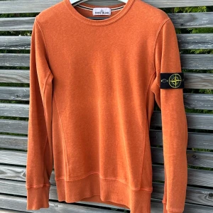 Orange sweatshirt från Stone Island - Säljer en orange stickad tröja från Stone Island med klassisk patch på ärmen. Tröjan har rund halsringning, sicket är perfekt och en 8,5/10