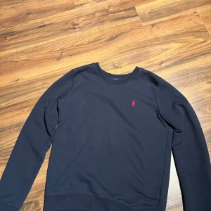 Mörkblå tröja från Polo Ralph Lauren - Mörkblå långärmad tröja från Polo Ralph Lauren i bomull. Klassisk crewneck med röd broderad logga på bröstet. Enkel och stilren design som passar perfekt till allting! (Om du har stora armar och använder storlek S så kan det vara ett problem för att den är ganska tight vid armen om du har stora armar)