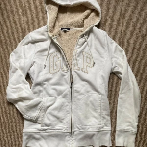 Teddy fodrard zip hoodie - Vit vintage hoodie från GAP med broderad logga framtill. Mjuk teddyfoder på insidan och huva med snören. Mycket mysig och gosig isolerad! Liknar päls hoodies, men detta är lättare att sköta om💕Dragkedja hela vägen och två fickor framtill. Perfekt för kyliga dagar och riktigt cozy vibes!😻Väldigt populär och sällsynt💋Så snygg y2k 2000s zip hoodie!! Storlek S, passar XS också. Använd några gånger, inga fel! Bara lite lite fläckig vid kragen framtill🩷Hör av dig vid frågor, pris kan diskuteras❤️
