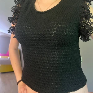 Svart spetsdetaljerad topp från Zara - Supersnygg svart topp från Zara med virkade detaljer och spets på axlarna. Toppen är ärmlös och har en tight passform med rund halsringning. Perfekt för dig som gillar spets och söta detaljer. (Liten i storleken)