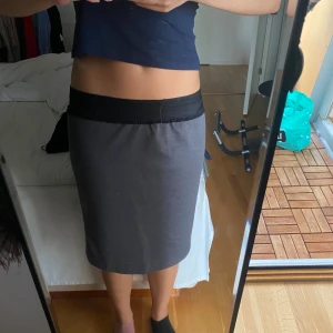 Grå pennkjol med svart midja - Säljer en stilren grå pennkjol med svart resår i midjan. Kjolen har en rak och tight passform som sitter snyggt och är enkel att matcha med olika toppar. Perfekt för dig som gillar en clean och enkel look.