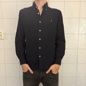 Mörkblå skjorta från Ralph Lauren - Klassisk mörkblå skjorta från Ralph Lauren med vit knappstängning och röd broderad logga på bröstet. Finns små små fläckar på insidan av skjortan men detta syns ej på! Jag på bilden är 184cm lång och väger 70kg. Nypris ligger på 1600 mitt pris 319! Hör av er vid funderingar.✌️✌️
