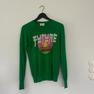 Grön stickad tröja From Future - Snygg grön stickad tröja från From Future med coolt retroinspirerat tryck i rosa, gult och rött framtill där det står 'FUTURE'. Tröjan har rund halsringning och långa ärmar. Sparsamt använd så i gott skick, det finns en liten fläck på magen, se bild som knappt syns och säkert går att tvätta bort! 