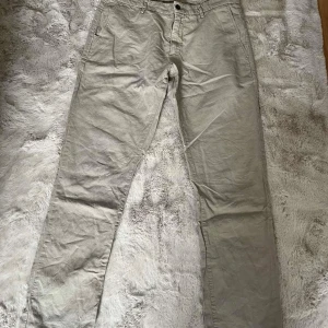 Beige chinos från NN07, storlek 32/32 - Snygga beige chinos från NN07 i storlek 32/32. Byxorna har raka ben, bälteshällor och klassiska fickor både fram och bak. Tillverkade i bomull för en skön och avslappnad känsla. Perfekta för en clean och stilren look.