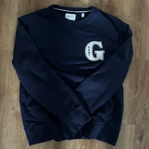 Mörkblå sweatshirt från Gant - Snygg mörkblå sweatshirt från Gant med stort broderat G på bröstet. Klassisk rund halsringning och långa ärmar. Tillverkad i mjuk bomull som är skön att ha på sig. Perfekt för en avslappnad och stilren look. Knappt änvänd kontakta för mer info 🔥