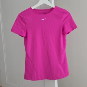 Rosa Nike Dri-Fit t-shirt - Nike Dri-Fit t-shirt i stark rosa färg med klassisk vit swoosh-logga på bröstet. T-shirten har rund hals och korta ärmar, perfekt för dig som gillar sportig och bekväm stil. Materialet är lätt och andas, vilket gör den grym för träning.Nyskick💕