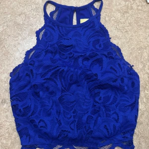 Kornblå spetsig croppad linnetopp - Snygg croppad linnetopp i blå spets med högt skuren hals. Storlek 32 från H&M, aldrig använt. 