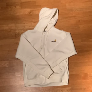 Carhartt zip hoodie - Säljer en helt ny creamfärgad hoodie från Carhartt med dragkedja framtill och huva med snörning. Endast använd 1 gång. Den är lite OVERSIZED (Se bild). Nypris 1350, öppen för prisförslag. Skriv vid minsta lilla fundering