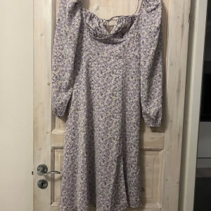 Ljuslila blommig klänning Adoore - Supersöt ljuslila klänning med små blommor, långa ärmar och snörning i ryggen. Klänningen har en avslappnad passform och offshoulder-skärning som ger en romantisk vibe. Perfekt för vår och sommar! Prislapp finns kvar 