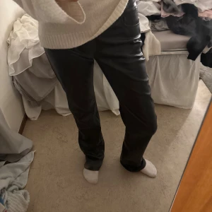 Svarta skinnbyxor från BikBok, stl 34 - Snygga svarta byxor i skinnimitation från BikBok. De har klassisk femficksdesign, raka ben och normal passform. Byxorna har knapp och dragkedja framtill och är perfekta för en trendig look.🤍