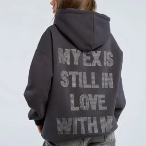 Svart hoodie med strass-text - Cool svart hoodie med stor huva och glittrig strass-text på ryggen: 'MY EX IS STILL IN LOVE WITH ME'. Oversized passform och mjukt material, perfekt för dig som vill sticka ut och visa att du har attityd.