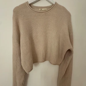 Beige croppad stickad tröja Pull&Bear - Säljer en beige croppad stickad tröja från Pull&Bear i storlek S. Tröjan har ribbad struktur, rund hals och långa ärmar. Perfekt för dig som gillar en chill och trendig look med lite loose passform.