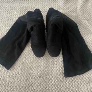Svarta mockastövlar med klack - Säljer ett par svarta stövlar i mocka med bred klack och rund tå. Skorna har dragkedja på insidan för enkel påtagning och en stilren, minimalistisk look. Perfekta för dig som vill ha en edgy och trendig vibe till din outfit.
