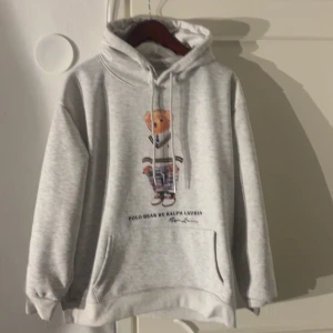 Grå hoodie Polo Bear från Ralph Lauren - Säljer en grå hoodie från Ralph Lauren med den ikoniska Polo Bear-trycket på bröstet. Riktigt skön och riktigt snygg, enda problemet är att den är lite liten i huvan! Hör av er vid frågor