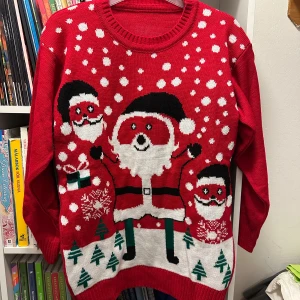 Röd jultröja med tomtemotiv strl: M - Rolig röd stickad jultröja med stora tomtar, snöflingor och granar. Tröjan har rund halsringning och långa ärmar. Perfekt för att sticka ut på julmiddagen eller luciafirandet!