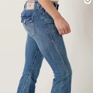 True Religion jeans - Säljer ett par blå jeans från True Religion med bootcut-modell. Jeansen har klassiska kontrastsömmar, snygga fickdetaljer med knappar och logopatch bak. En knapp har låsbat där bak men inget man tänker på, därav priset. Något slita längst ner.