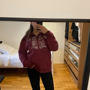 Vinröd hoodiefrån One of One - Säljer en vinröd hoodie från One of One i storlek medium. Tröjan har dragkedja, huva med snörning och coolt strassmönster framtill med texten 'The Wolf of Moselacke'. Perfekt för dig som gillar streetstyle och vill sticka ut. Tröjan har en defekt som syns i sista bild