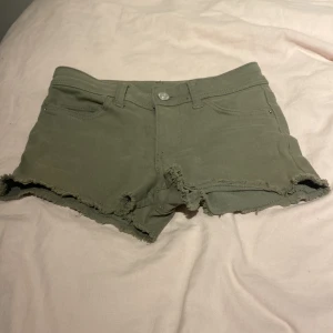 Olivgröna jeansshorts med fransig kant - Snygga olivgröna jeansshorts med fransig kant och klassisk femficksmodell. De har låg midja och råa kanter för en avslappnad vibe. Perfekta för varma dagar och enkel att matcha med allt.
