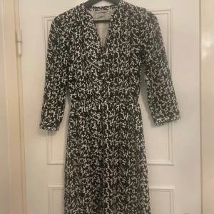 H&M klänning i svart/vitt/blått med knappar, - H&M klänning i svart/vitt/blått med knappar, storlek 34. Fina tygbeklädda knappar från midjan och upp till halsen, där du kan välja att han klänningen helt stängd eller med urringning.   Mycket fint skick.