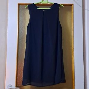 Mörkblå ärmlös klänning Atmosphere - En stilren mörkblå ärmlös klänning från Atmosphere. Klänningen är kort, har rund halsringning och en enkel, rak passform. Materialet känns lätt och flowy, perfekt för dig som gillar minimalistisk stil. Det finns små hällor i sidorna för eventuellt bälte.