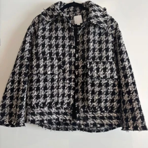Rutig svartvit tweed jacka från H&M - Snygg svartvit rutig tweed jacka från H&M med grov struktur och stora fickor framtill. Jackan har klassisk krage, två fickor och är tillverkad i ett tjockare tyg som ger en cool och trendig look. Perfekt för dig som gillar statement-plagg.