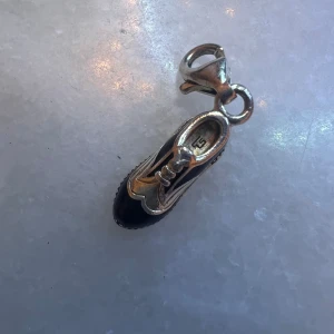 Thomas Sabo sko-berlock i silver och svart - Unik berlock från Thomas Sabo formad som en sko i silver med svarta detaljer. Snygg och detaljerad design med snörningsmönster och karbinhake för enkel fastsättning på armband eller halsband. Perfekt accessoar för dig som gillar personliga smycken.