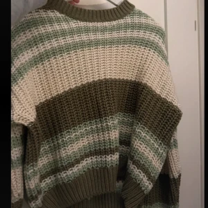 Randig stickad tröja från Noisy May - Tröjan har breda ränder i olivgrönt, beige och vitt, med grov ribbad kant vid hals, ärmslut och nederkant. Använd enstaka gång.