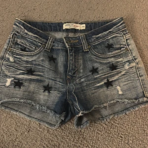 Blå jeansshorts med svarta stjärnor - Snygga blå jeansshorts från Detroit by Lindex med slitna detaljer och svarta stjärnor broderade på fram- och bakfickor. Shortsen har fransig kant nedtill och klassisk femficksdesign. Perfekt för dig som gillar en cool och avslappnad stil. 💞