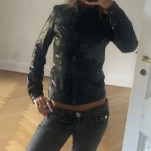 Svart skinnjacka med knappar - Snygg svart skinnjacka med klassisk passform och knappar framtill. Jackan har långa ärmar och en stilren look som passar perfekt till jeans eller kjol. Materialet är äkta skinn och jackan har en tidlös design.