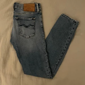 Replay ljusblå jeans - Säljer ett par snygga ljusblå Replay New Luz jeans med klassisk femficksdesign och tydliga slitningar. Jeansen har raka ben, normal passform och är tillverkade i mjukt denim med Replay-logga på bakfickan och läderpatch i midjan.                                📏 Storlek: W27 ✨ Skick: Mycket bra skick, sparsamt använda. 🧵 Material: Bomull med stretch för bekväm passform.                                                                                  ✅ Pris kan diskuteras