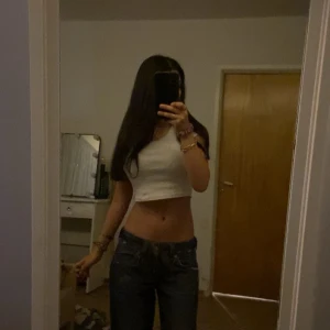 Tommy Hilfiger bootcut jeans blå denim - Säljer ett par blå bootcut jeans från Tommy Hilfiger Denim med slitna detaljer och klassisk Hilfiger-logga på fickan. Jeansen har låg midja, orange kontrastsömmar och är tillverkade i robust denim. Perfekta för dig som gillar en avslappnad och trendig look.